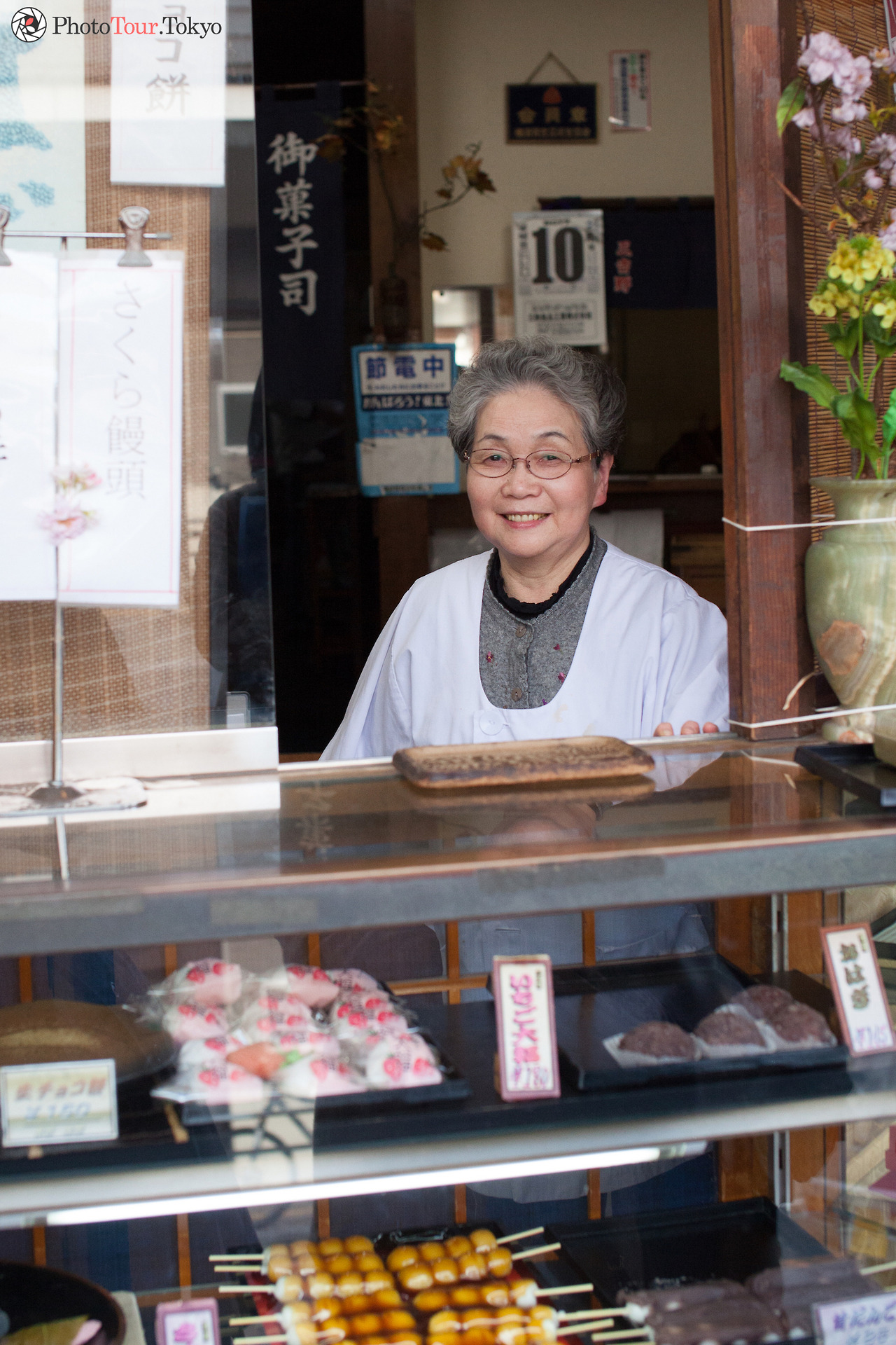 <p>PhotoTour.Tokyo in Yokosuka, Kanagawa. Smiling shopkeeper at the Japanese traditional sweets shop. In the photo you can see Ichigo Daifuku, Ohagi and Dango Yaki.</p>