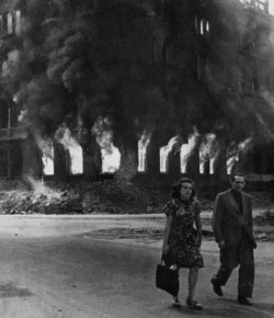 poetryconcrete:A German couple walks past a burning building