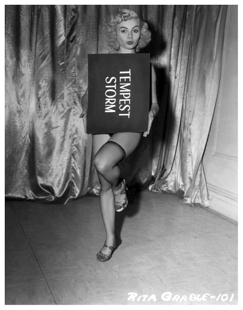 Rita Grable has fun with Tempest Storm’s title card in this publicity still from Irving Klaw’s 1956 Burlesque Film: “BUXOM BEAUTEASE”..