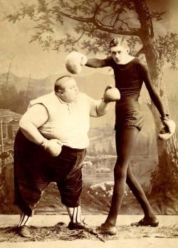 Two Victorian sideshow performers boxing – the fat man and