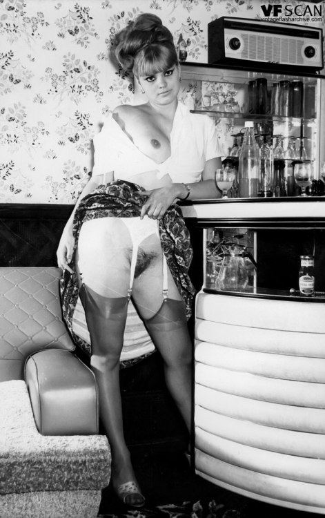 Pretty girl with 60’s beehive hairstyle poses by the cocktail bar in her nylon stockings and suspenders. 