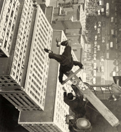 A man balancing on a piece of wood on the roof of a skyscraper,