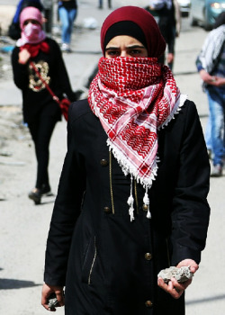 A Palestinian woman holds stones following a rally to mark International