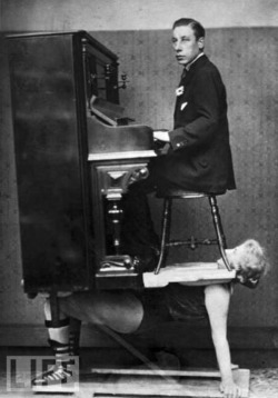 A circus strongwoman balances a piano and a pianist on her chest,