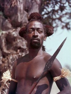 congo-mondele:  A Kuba hunter, ca. 1950, holds a spear and wears his hunting regalia, including armbands and a fur headdress. Kasai province, Belgian Congo (today DR Congo) | © Otto Lang 