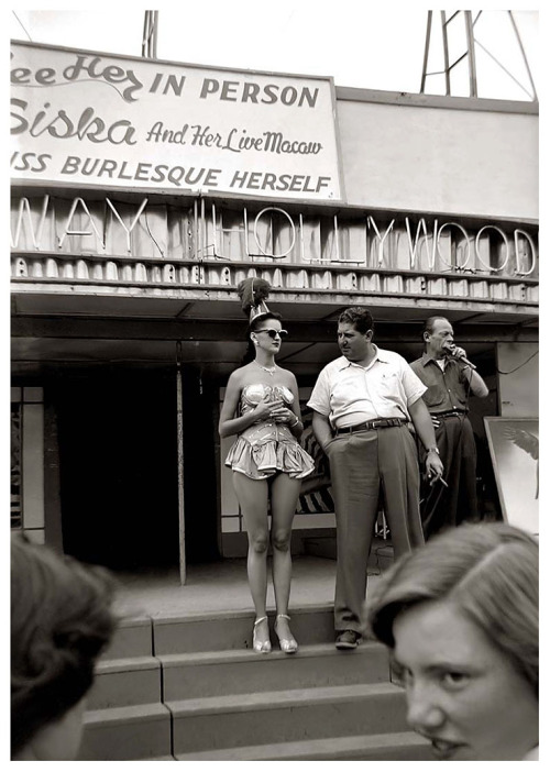 Vintage 50’s-era candid photo captures a pair of teenage girls taking in the spiel of a Carnival barker.. An unidentified showgirl presents herself on the Bally stage of a girlie-show headlined by “Miss Burlesque Herself”: Siska..