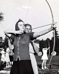 The coach helps a girl on the archery team with her aim, 1942.