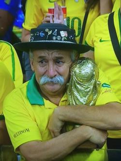 Old man with a mustache hugging a world cup while watching Brazil