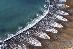 sixpenceee:  Waves create a striking pattern on a sandy beach