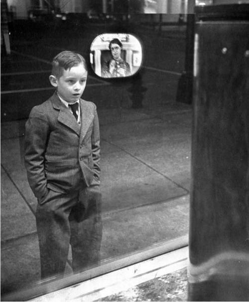 A boy watches television for the first time through a shop window,