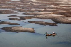 xne:  Two men row a boat past a partially dried-up riverbed on