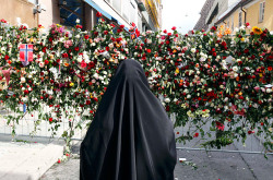 A Muslim woman stands in front of a sea of flowers placed outside