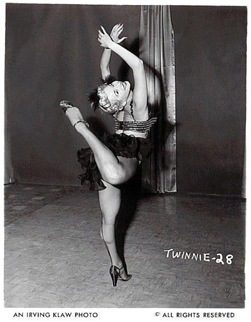 Twinnie Wallen kicks up her heel.. From a photo series shot by Irving Klaw, during the production of his films: ‘VARIETEASE’ and ‘TEASERAMA’..