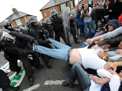 Police and rioters come together to help fat man out of trousers.