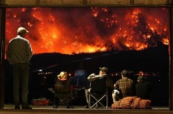 Grounded helicopter pilots watch as a forest fire rages on Mt.