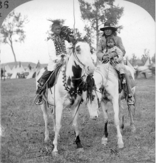 thebigkelu: A Native American Dakota Sioux man and boy pose mounted on horses outside their tepee ca