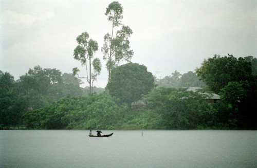 nadanzum: Ian Berry. BANGLADESH. Small wooden water taxi ferries a passenger sheltering from the mon