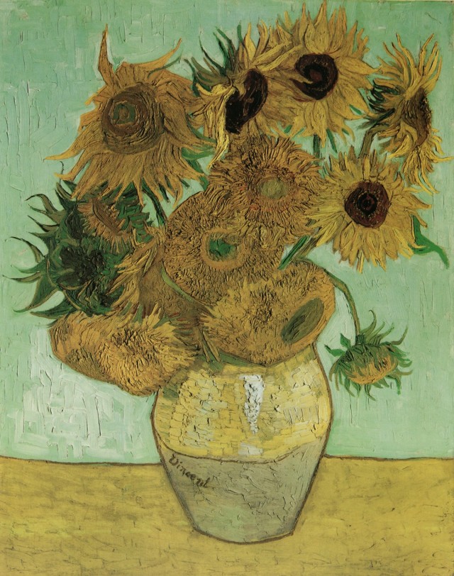 A bouquet of sunflowers in a vase against a pale green wall. 
