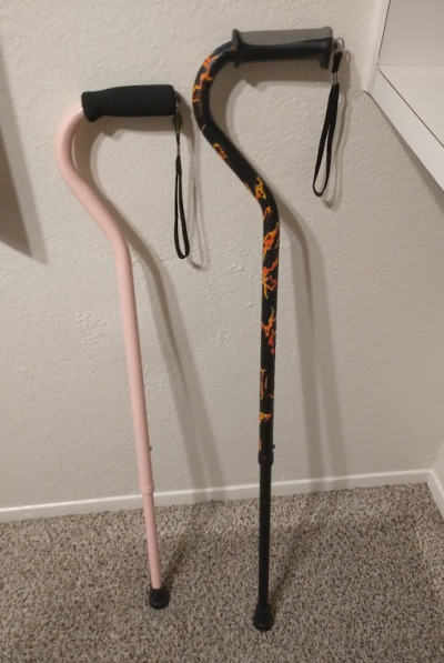 Two canes side by side. The one on the left is painted a light pink, and the one on the right is painted black with a fire/lava pattern.