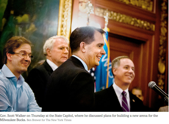 Gov. Scott Walker (R-WI), a white man, stands at a press conference surrounded by three additional white men. Another white man is visible in the corner by the door. This photograph originally appeared in The New York Times.