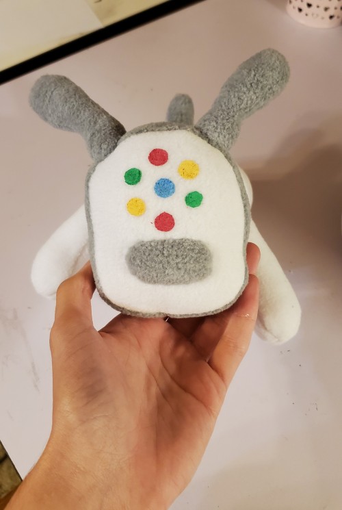 A photograph of a plush toy made to resemble an iDog. This one is white and facing the camera, with multicolored spots on the face.