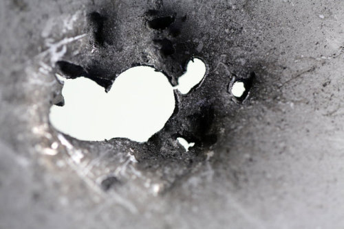 An aluminium plate, ripped inwards by a single sand grain-sized fleck of aluminium oxide shot at it 