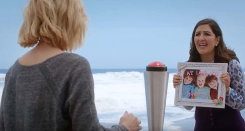 A screenshot from The Good Place; Janet in fake distress, showing Eleanor a photo of her fake children as Eleanor prepares to press that button that will kill her.