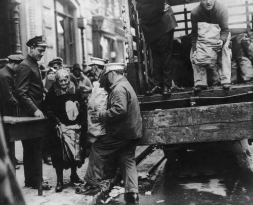 An old woman receives her Thanksgiving ration of food as other hungry people wait in line for theirs