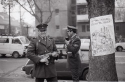 waskgr:  Carabinero armado con una metralleta, sonriéndole a la cámara, mientras que a su izquierda hay una afiche en contra de los crímenes en contra del pueblo.