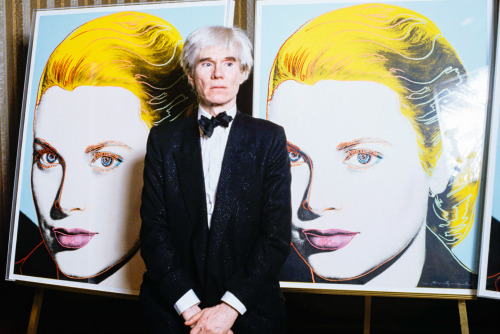  Andy Warhol stands in front of a limited edition serigraph of Princess Grace of Monaco to benefit t