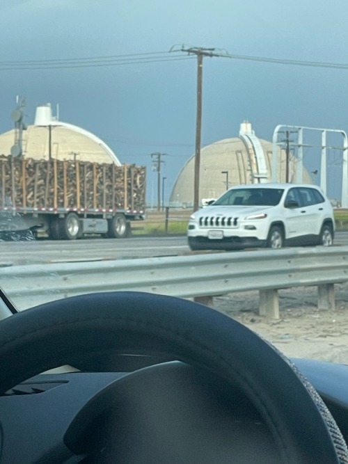 picture through a cars windshield of two concrete domes with some cars driving in front of them
