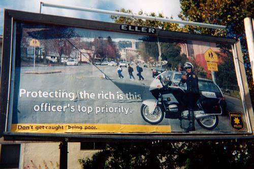 ragemovement:  Subvertising in California! “Protecting the rich is this officer’s