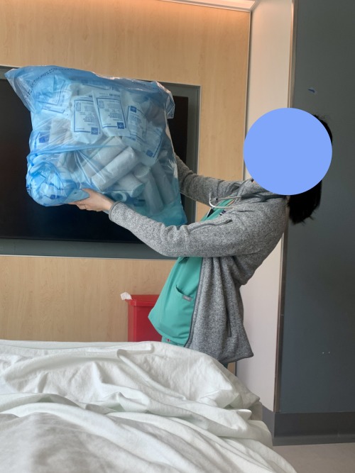 [Image description: A nurse brings a large blue plastic bag of various supplies to my hospital bed. 