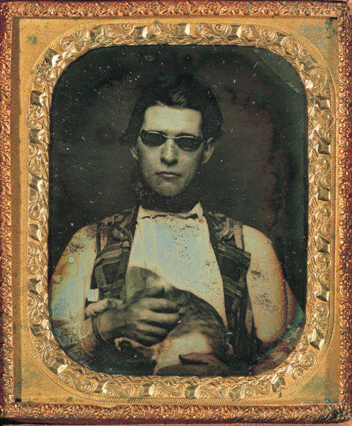 Daguerreotype of a blind man wearing tinted glasses, holding a cat, c. 1850.