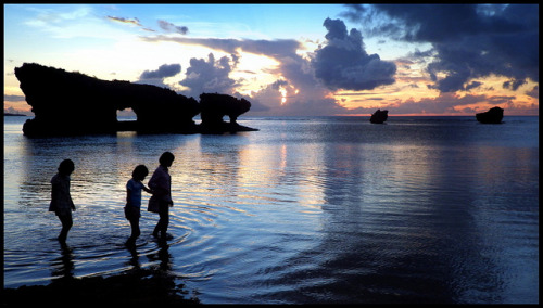 KIDS AND THEIR MOM IN SILHOUETTE AS THEY WALK ACROSS THE SUNSET TIDAL FLATS in OKINAWA