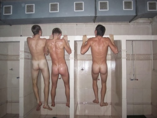 Young naked footballers bench press in the showers