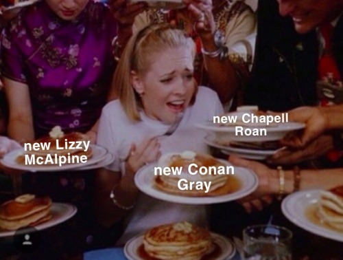 A person being surrounded and fed stacks of pancakes. Three of the stacks are labeled "new Chapell Roan," "new Conan Gray," and "new Lizzy McAlpine."