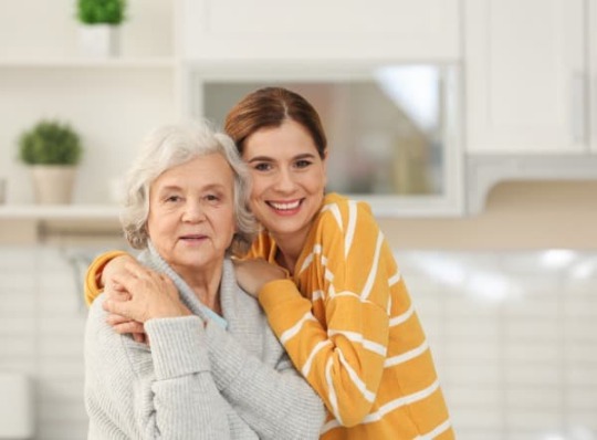 Caregiver, younger woman side-hugging older woman
