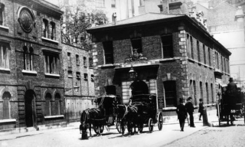 Scotland Yard [left] and horse-drawn carriages outside the Public Carriage Office (London, c. 1875).