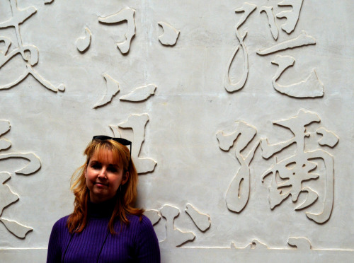 Cathy standing next to a wall full of Chinese characters located in the National Museum of Chinese W