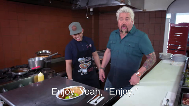 92% sure it's Guy Fieri and woman preparing food in a kitchen. Caption: Enjoy. Yeah, "Enjoy."