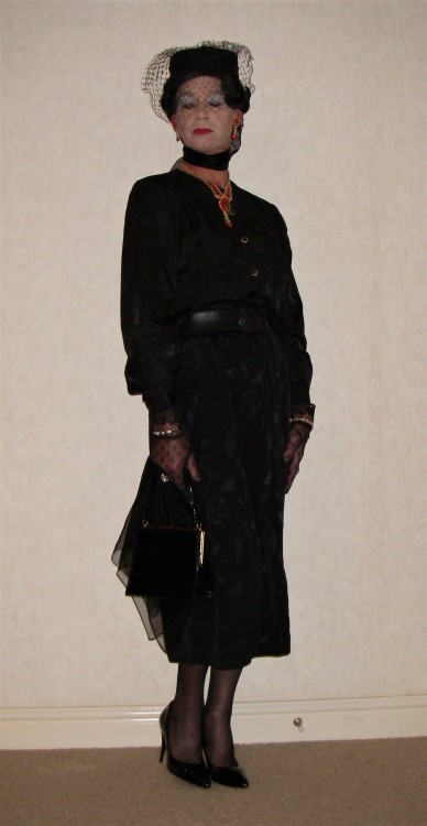 A black satin blouse with satin skirt. Wearing a veiled hat and with chiffon scarves and a handbag