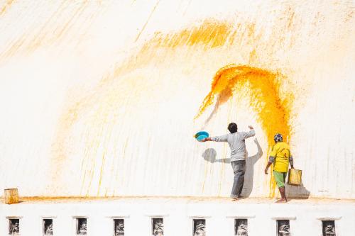 Graceful throwing of yellow paint on the Boudhanath Stupa in Kathmandu, Nepal. The saffron based wat