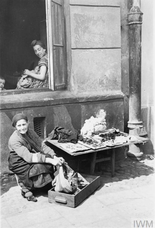 Warsaw Ghetto (Poland, 1941):An elderly Jewish woman selling her scarce possessions in the street.A 