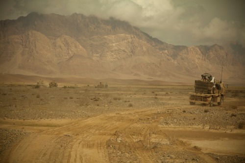 Majestic mountains, dangerous desert. Coalition force tactical vehicles move across the desert depar