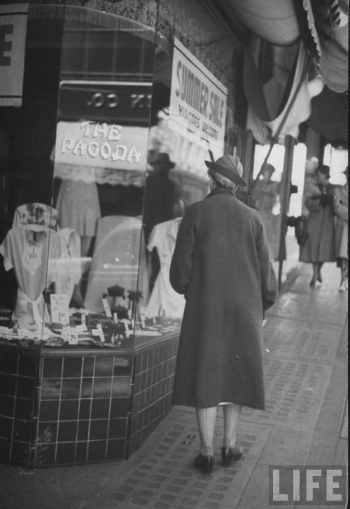 A woman window shopping as she walks along the sidewalk in a Californian Chinatown, 1941. Photograph