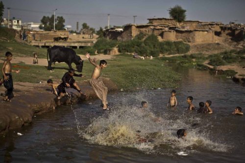 An Afghan refugee boy jumps into the water, while he and others swim in a polluted stream to cool of