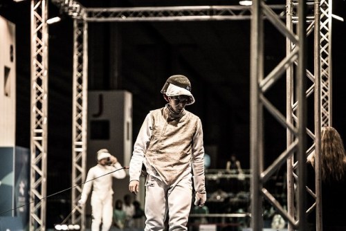 [ID: a foil fencer walking on strip, framed by metal crossbeams.]Fencing at the 2017 Summer Universi