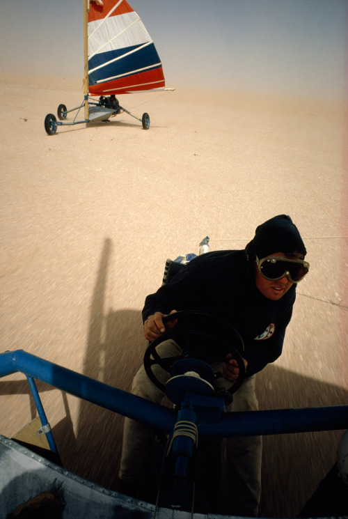 A land yacht pilot grips one wheel to steer and one to control sails in the Sahara Desert, Mauritani