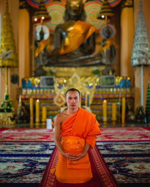 A Buddhist monk kneels in front of the large, bronze Phra Ong...